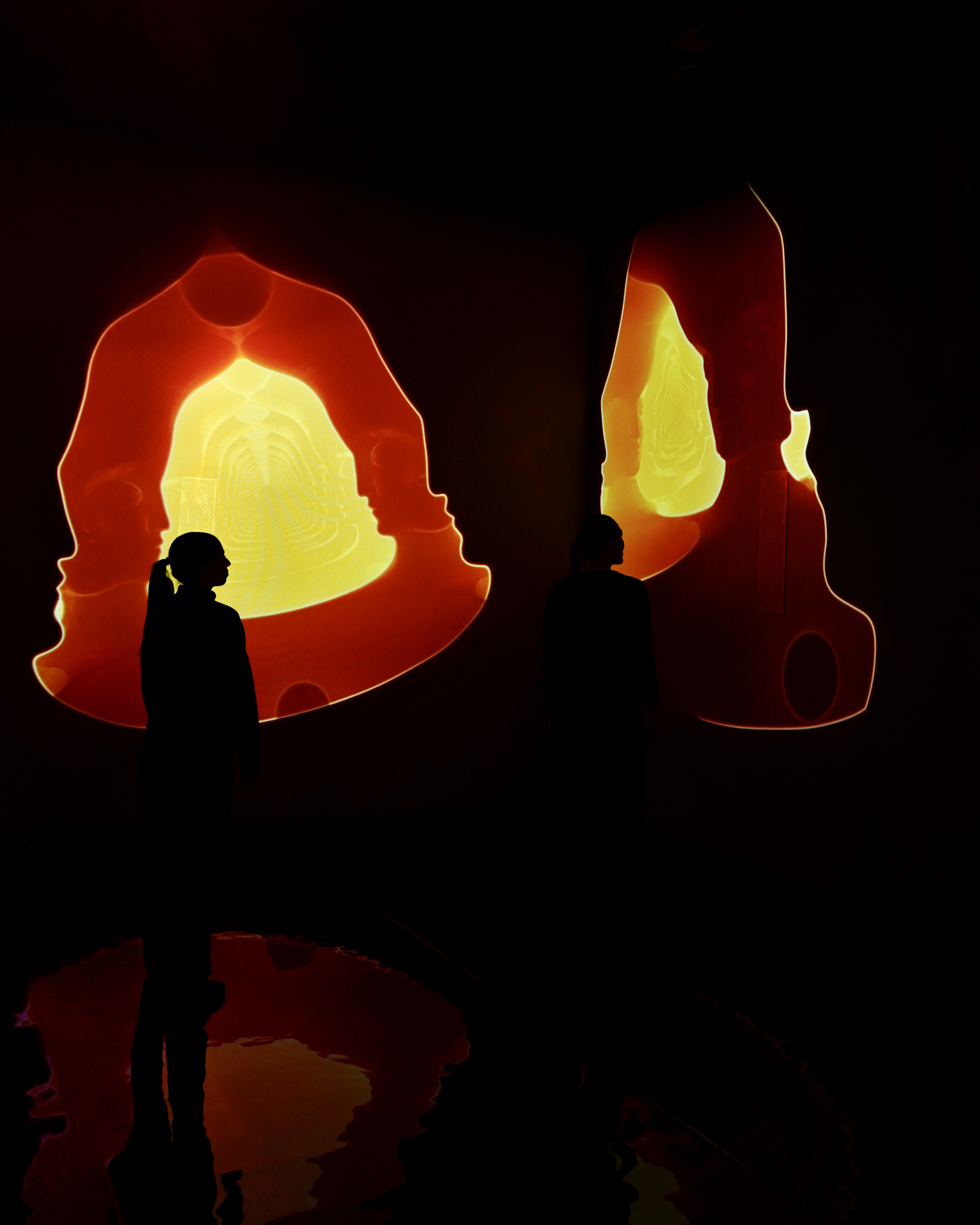 Two visitors silhouetted against glowing red cave portals